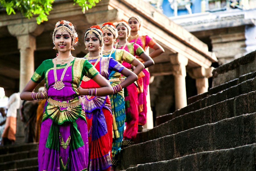 Five Bharatanatyam dancers in colourful traditional costume posing on temple steps